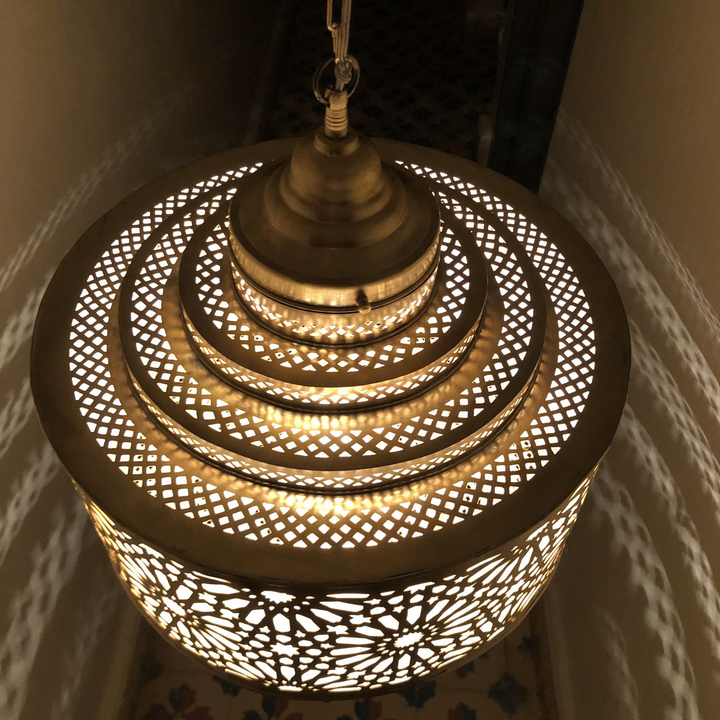 Ibrahim Parchment brass lamp above a dining table with gentle illumination and Moroccan decorative character.