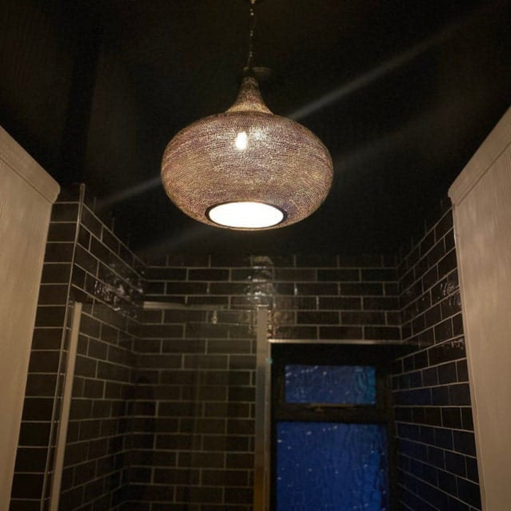 Iman brass pendant light with artisan metal texture spreading calm decorative glow across nearby ceiling and wall areas.