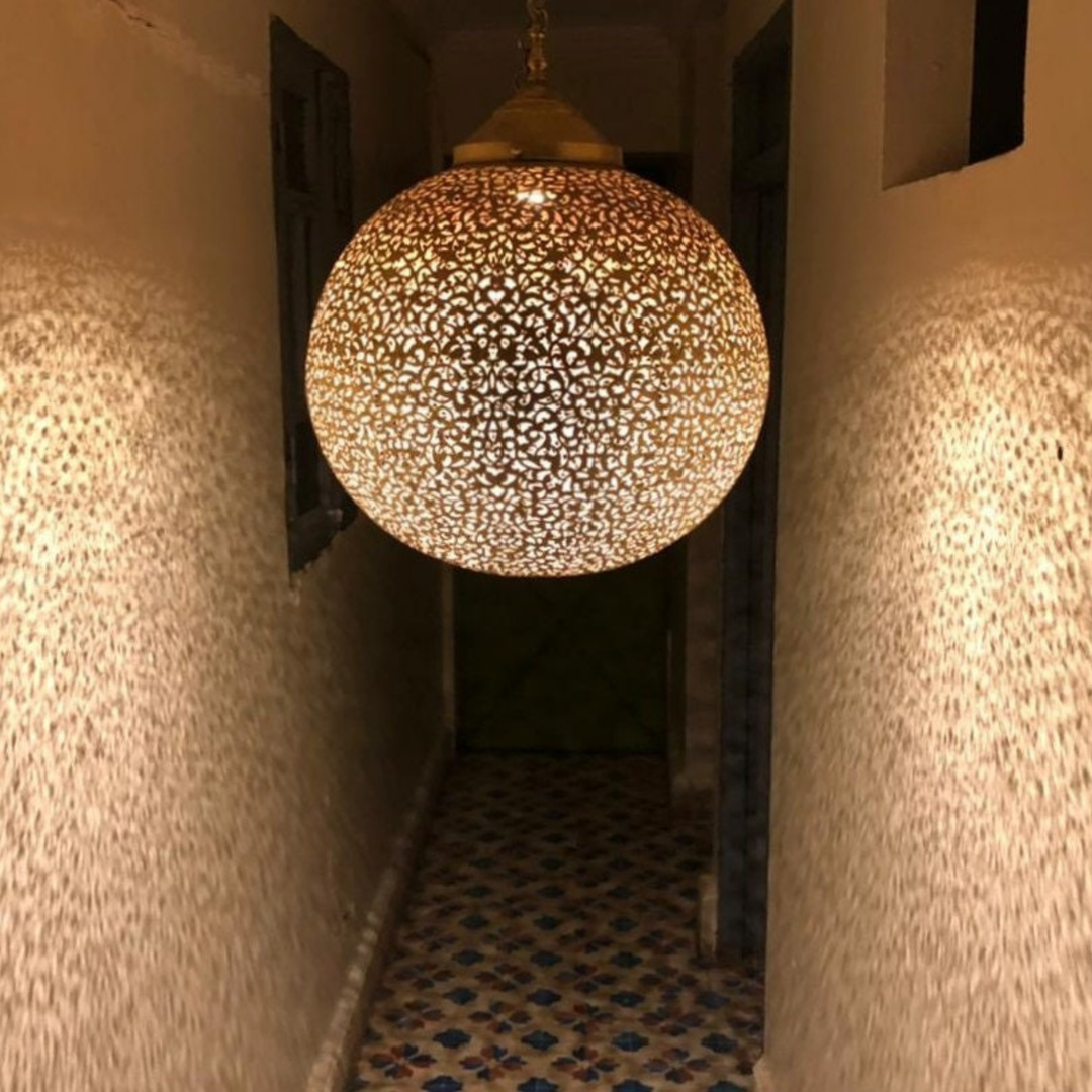 Koora brass ceiling light with globe pendant shape casting warm patterned reflections across a bedroom ceiling.