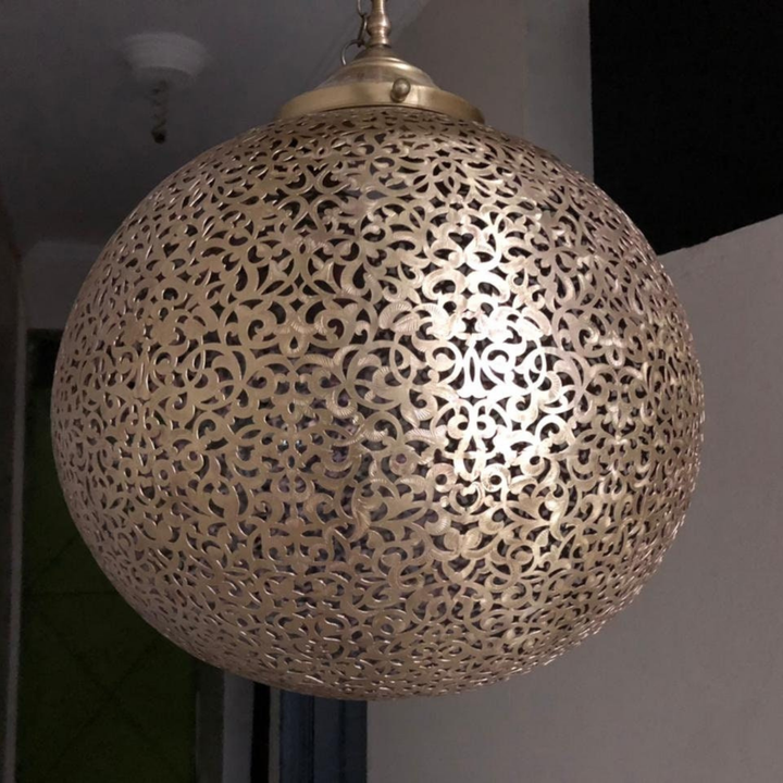 Koora globe pendant lamp above a dining table with golden brass finish and soft decorative overhead glow.