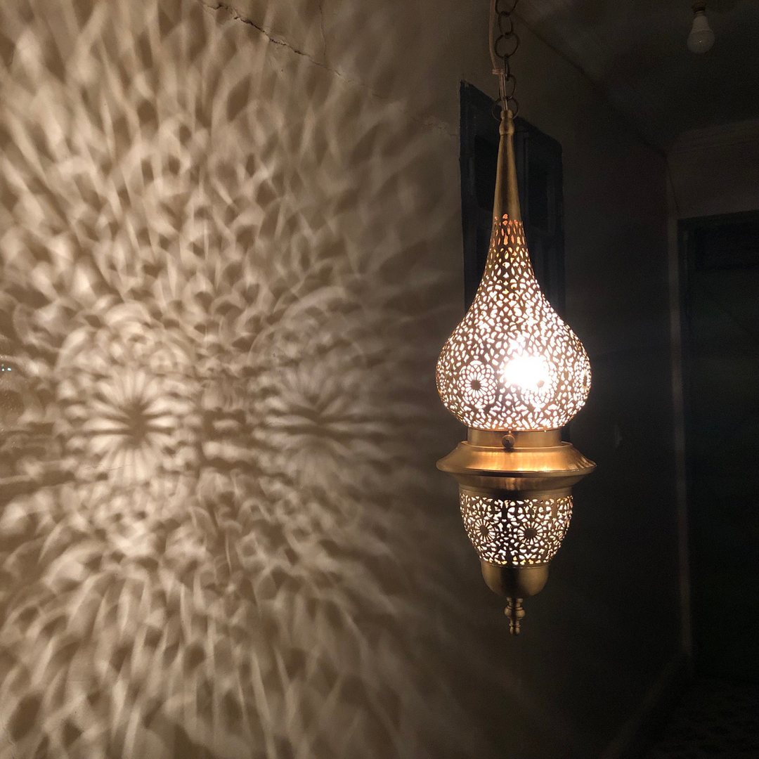 Nur brass ceiling light with pierced brass shade creating warm shadow patterns across a cozy bedroom ceiling.