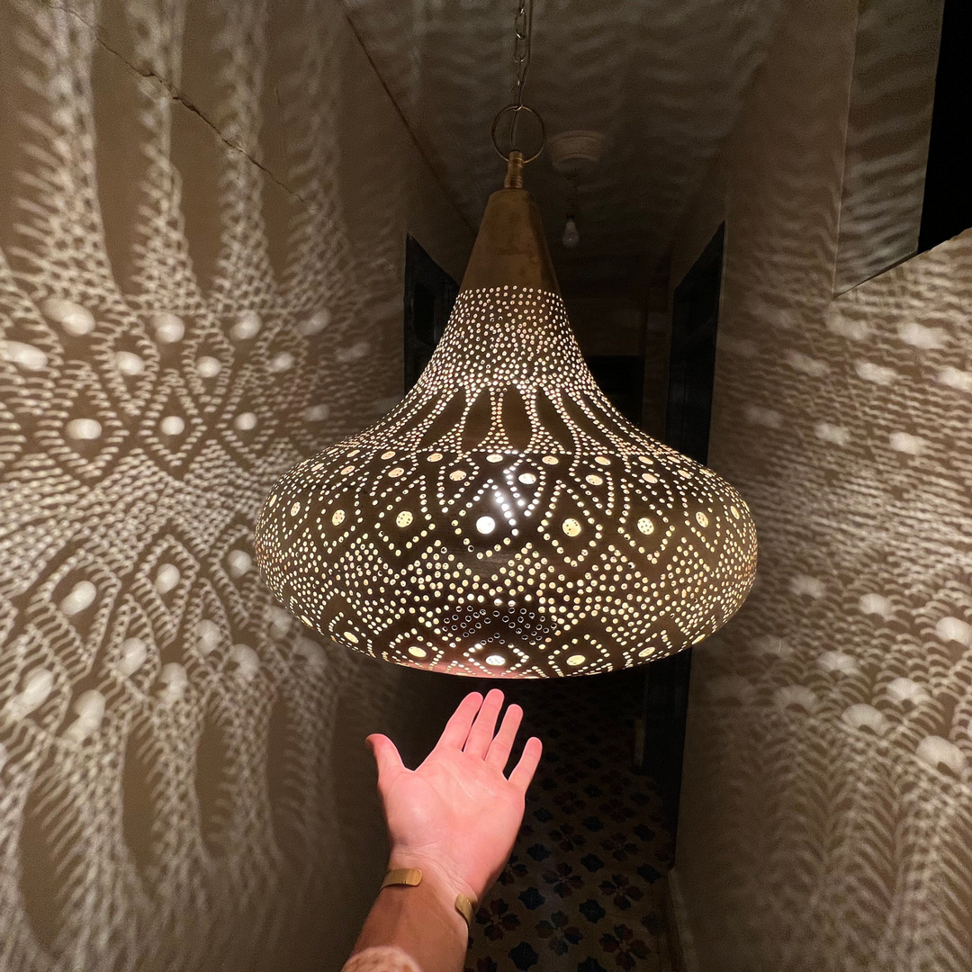 Terboch brass ceiling light with sculpted hanging shade creating warm patterned reflections across a bedroom ceiling.