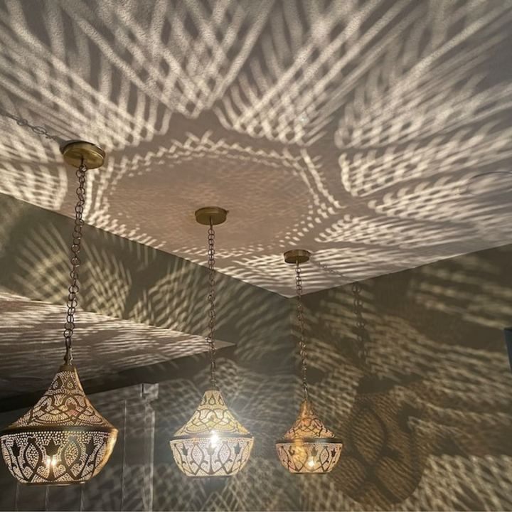 Yussra brass hanging light with decorative openwork texture spreading warm patterned glow across walls and ceiling areas.