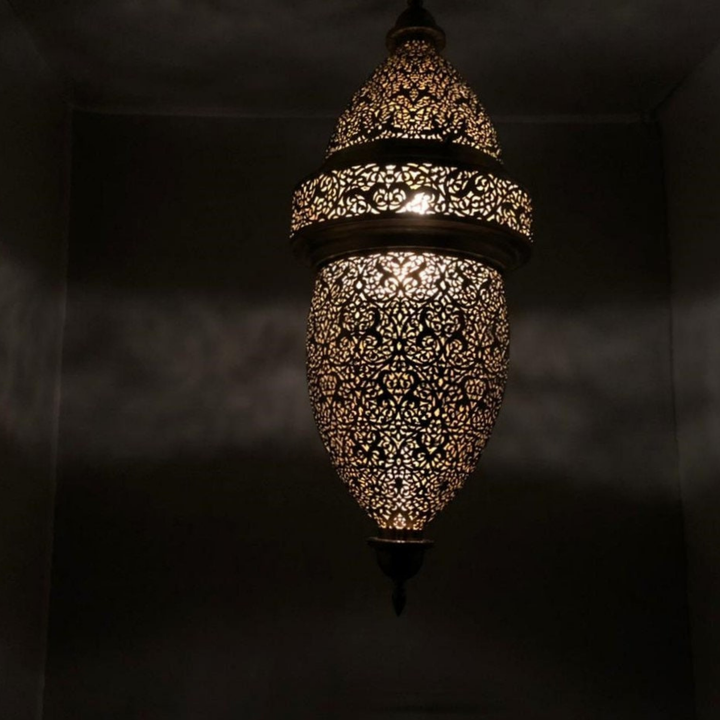 Hilal hanging brass lamp casting delicate reflections through pierced metal across a calm entryway wall.