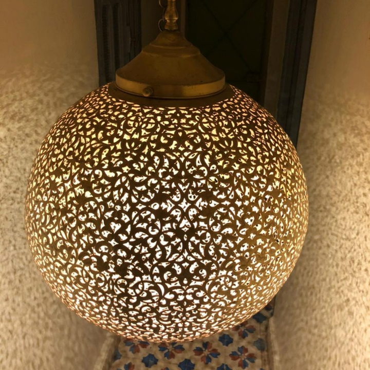 Side profile of Koora ceiling light showing ball shaped brass shade, neat rim, and suspended lamp silhouette.