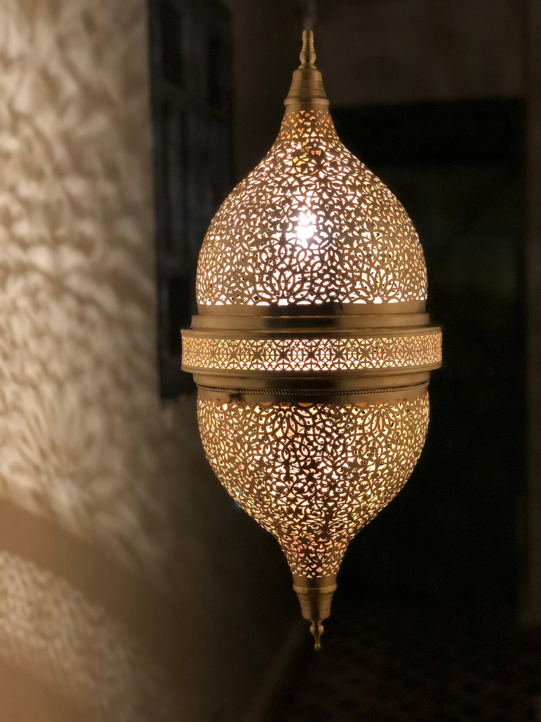 Handcrafted Moroccan brass wall sconce with intricate cutouts, illuminated casting warm shadows for hotel and restaurant projects.⁠