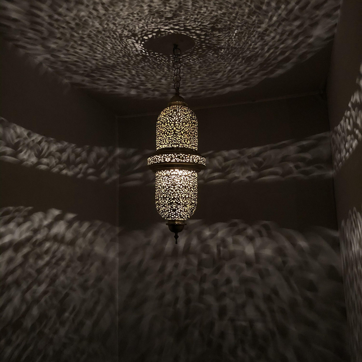 Salim brass lamp shade above a dining table with golden finish, decorative cutwork, and soft overhead glow.