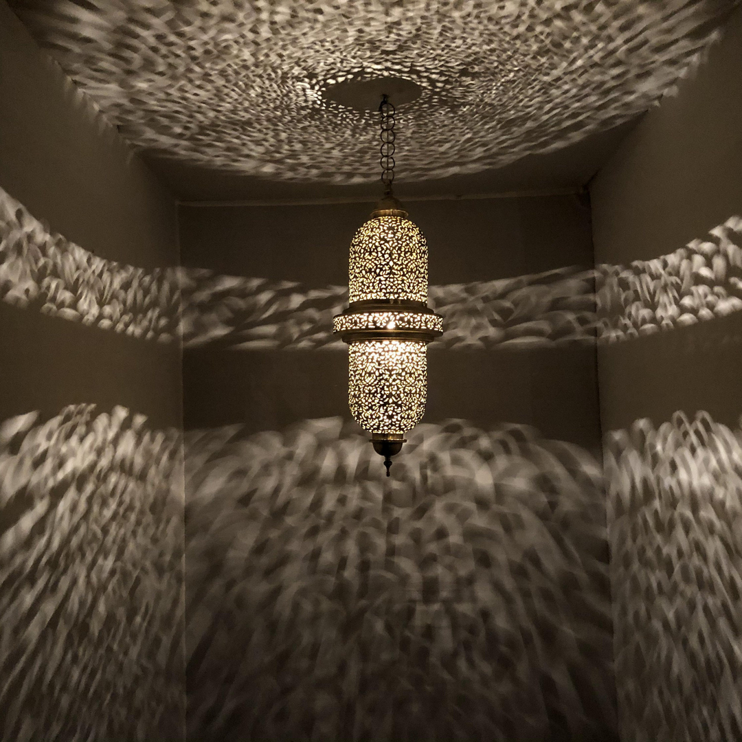 Salim hanging brass fixture casting gentle dotted reflections through perforated metal across an entry hallway.
